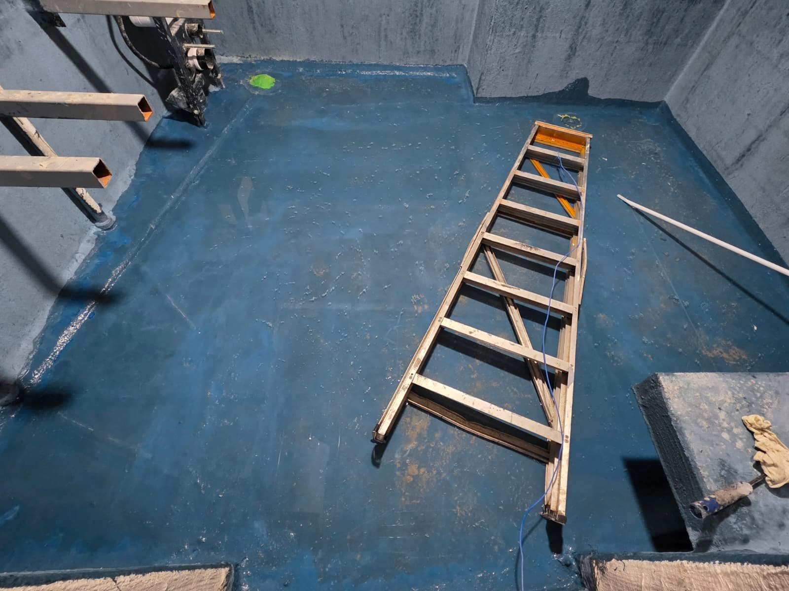 Blue waterproofing membrane applied across wet-area floor with roller